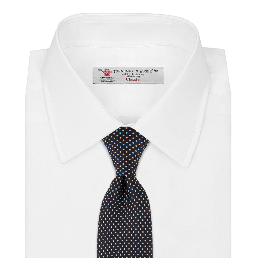 The Turnbull & Asser Black and White Small Spot Printed Silk Tie, shown rolled against a white background, features a subtle polka dot pattern—an ideal accessory for any office shirt.