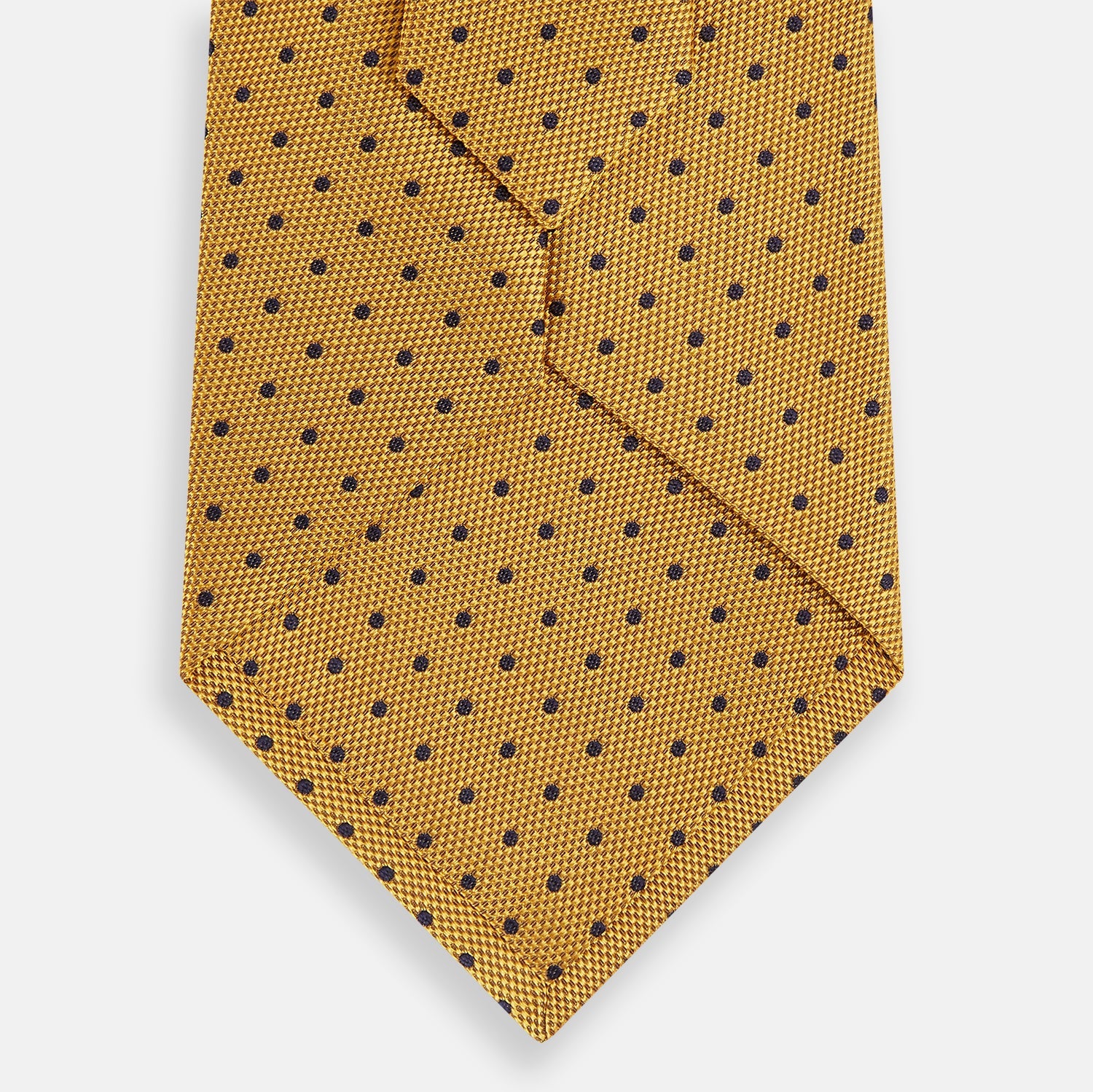 View 3 of product The Turnbull & Asser Navy and Yellow Micro Dot Silk Tie features evenly spaced dark blue micro dots on yellow silk, rolled and displayed on a white background—an elegant accessory for any occasion.