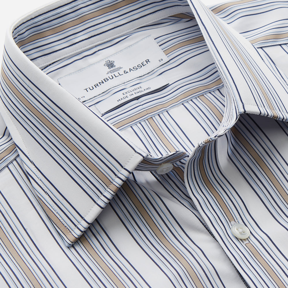 The Turnbull & Asser Sand Multi Stripe Regular Fit Shirt features a T&A collar, 3 button cuffs, and vertical blue, white, and light brown stripes. The shirt is shown neatly laid flat on a white background.