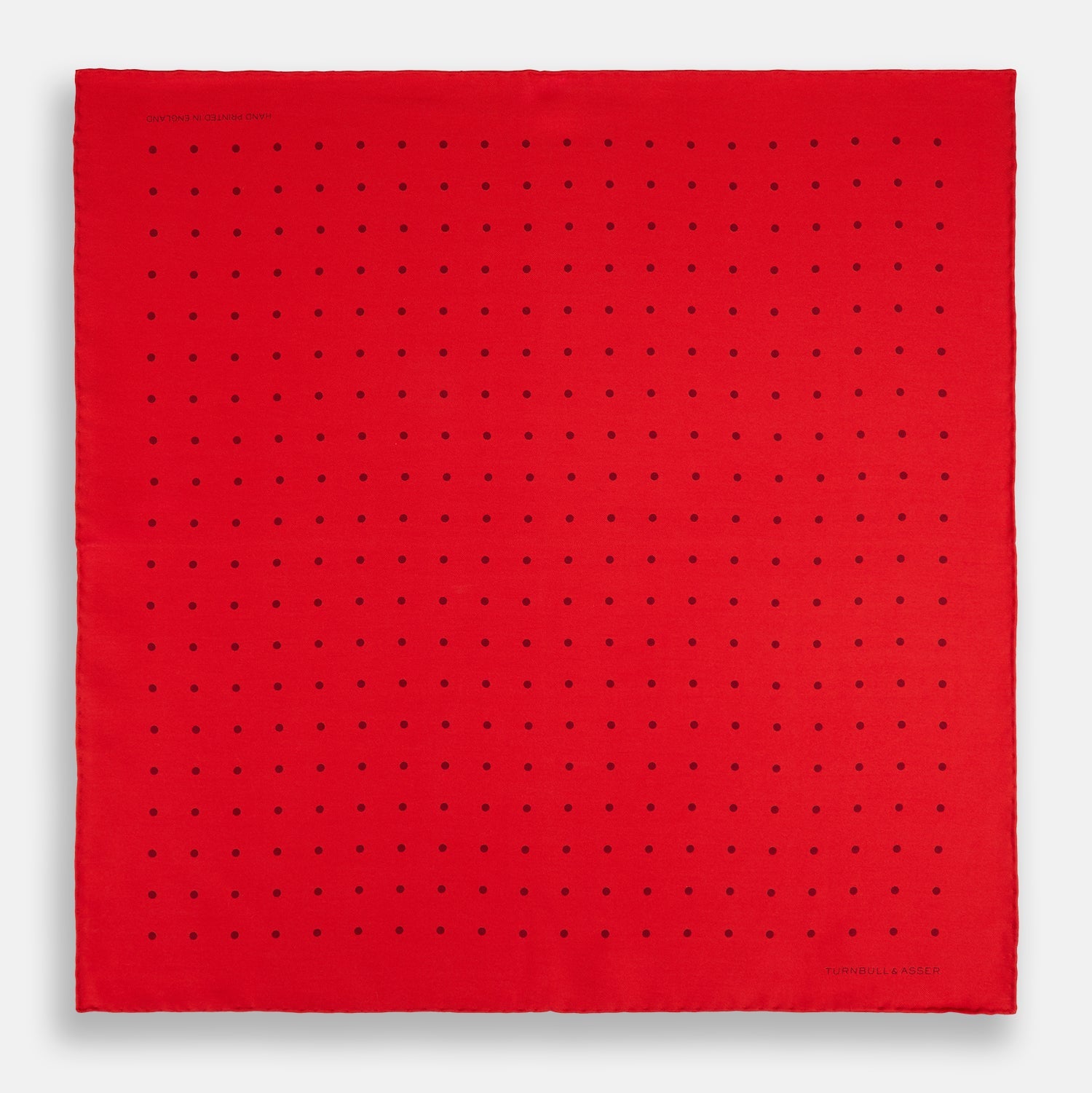 View 4 of product The Turnbull & Asser Red and Burgundy Spot Silk Pocket Square features evenly spaced small spots and the brand logo in the bottom right corner—perfect for formal wear. One corner is folded to show the reverse side.