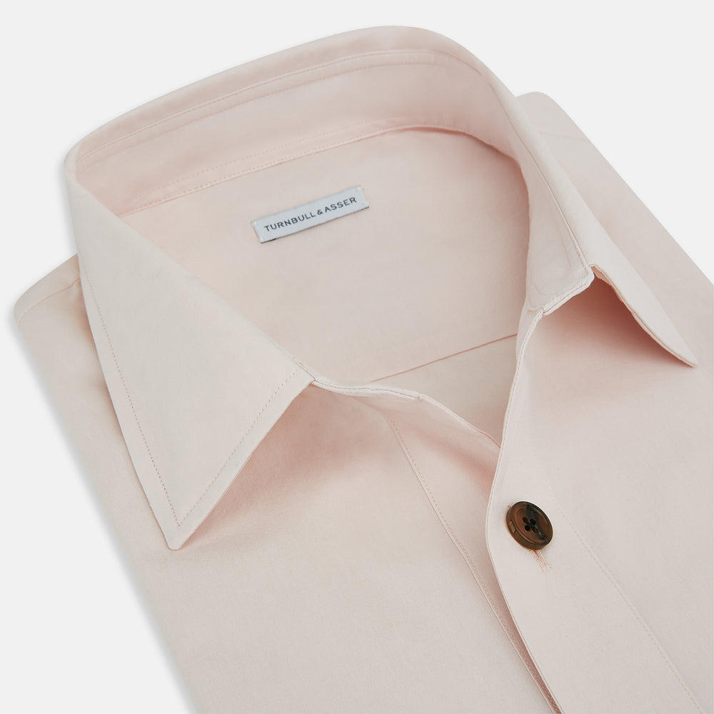 The Turnbull & Asser Pale Pink Hyde Overshirt is a long-sleeve, sanforised cotton button-up with a left chest pocket and dark buttons, shown laid flat on a white background.