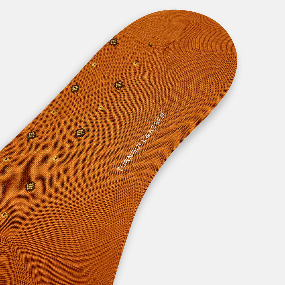 Turnbull & Asser’s Orange Patterned Mid-Length Socks, made from soft Egyptian cotton and featuring a ribbed cuff with small black and yellow geometric dots, are displayed against a plain white background.