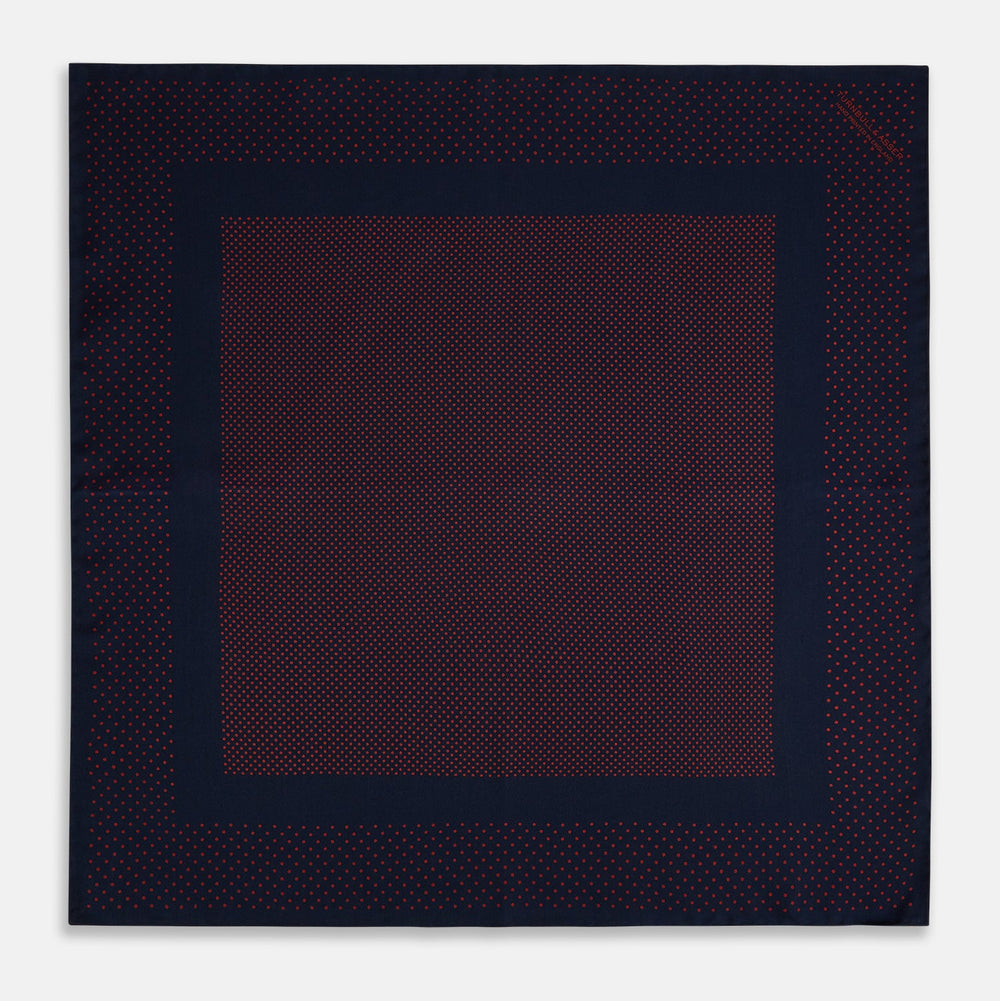 The Turnbull & Asser Navy and Red Dot Silk Pocket Square features a dark navy blue base with small red polka dots on the border and inner pattern, all handmade and neatly folded.