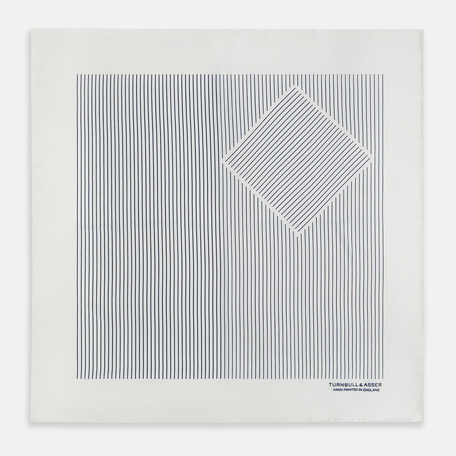 View 4 of product The White Stripe Silk Pocket Square by Turnbull & Asser features vertical navy pinstripes and “TURNBULL & ASSER HAND PRINTED IN ENGLAND” in blue at the lower right, with one corner neatly folded for a classic British look.