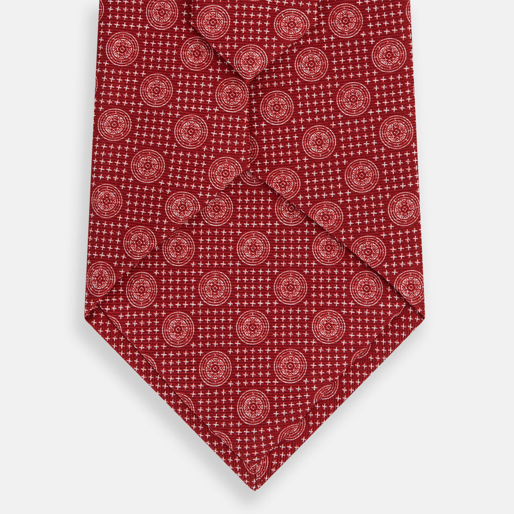 The Turnbull & Asser Red Medallion Silk Tie features a repeating white geometric medallion motif on vibrant red silk, shown against a plain white background.