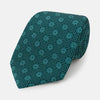 View 1 of product The Forest Green Medallion Printed Silk Tie by Turnbull & Asser features a repeating medallion pattern in lighter green tones, crafted from English silk and shown rolled up on a plain white background.