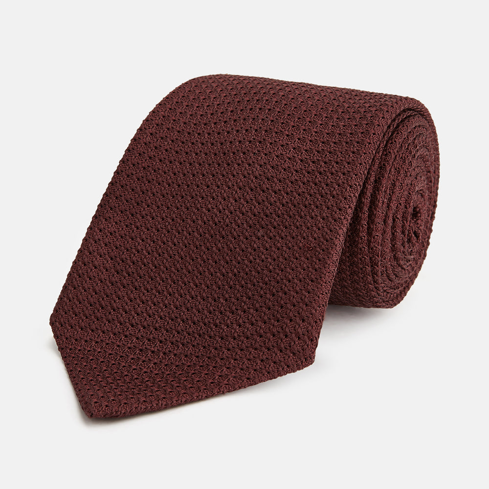The Turnbull & Asser Dark Red Knitted Tie, featuring a textured finish, is shown rolled up against a white background—a stylish and versatile accessory ideal for the modern gentleman.