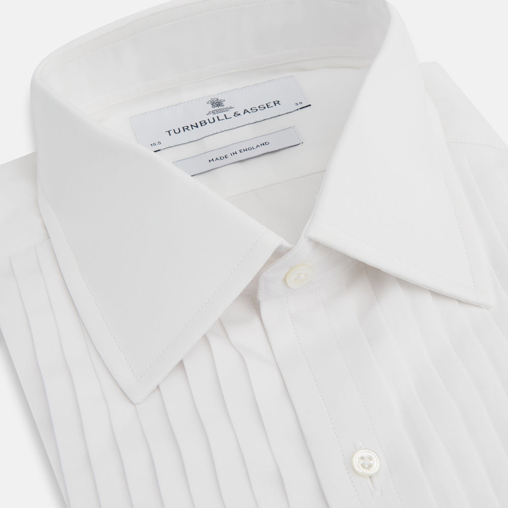 The Turnbull & Asser White Pleated Cotton Dress Shirt features a T&A collar, pleated front, double cuffs, and a button-down front, shown laid flat against a white background.