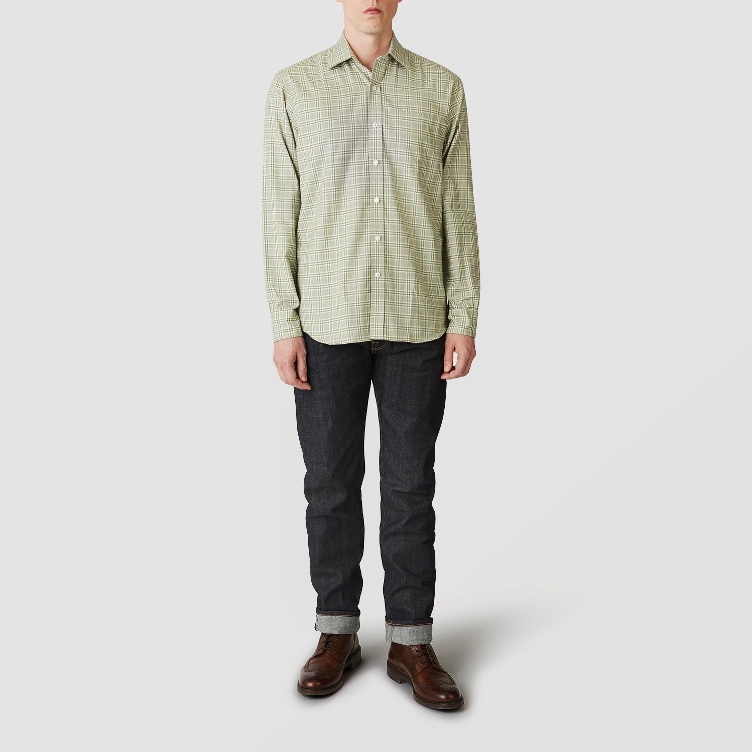 View 1 of product A person faces forward wearing the Turnbull & Asser Green Check Weekend Fit Shirt with Derby Collar and 1-Button Cuffs, dark cuffed jeans, and brown leather shoes against a plain light gray background.
