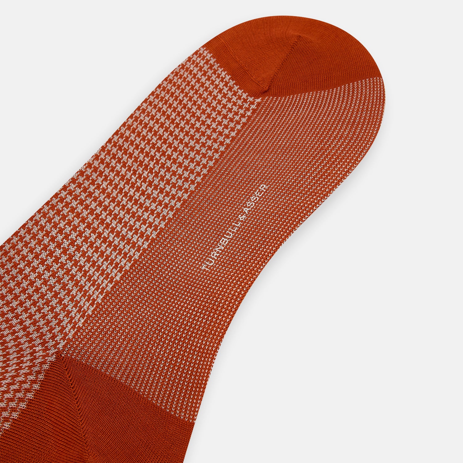 View 3 of product The Turnbull & Asser SOCKS LONG COTTON HOUNDSTOOTH ROSE is a single over-the-calf sock in rusty orange with a white houndstooth pattern and solid orange toe, heel, and cuff, shown on a plain white background.