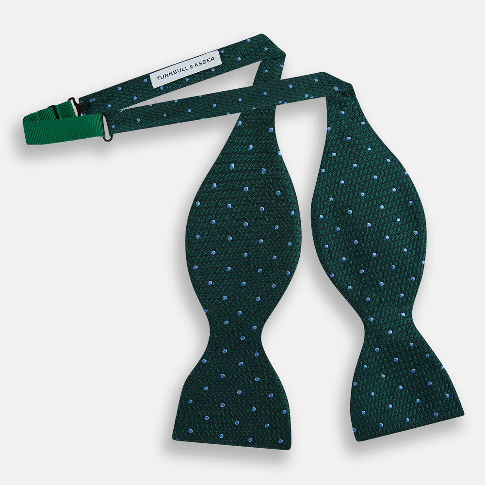 The Turnbull & Asser Forest Green and Sky Blue Spot Houndstooth Silk Bow Tie features a textured pattern with light blue polka dots, shown against a plain white background.