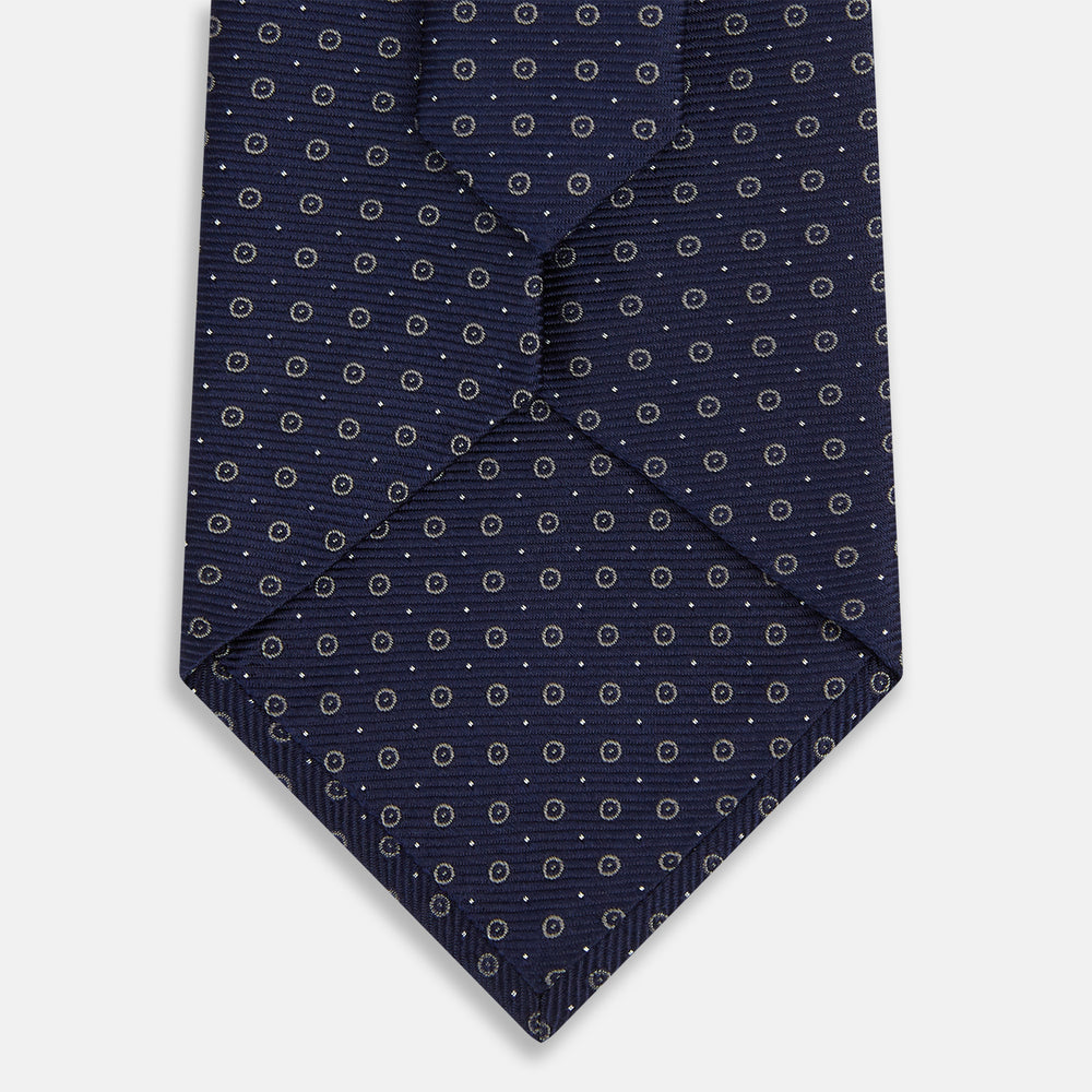 The Turnbull & Asser Navy and Grey Circle Silk Tie, featuring a refined pattern of evenly spaced circles, is elegantly displayed rolled up on a white background—an excellent option for modern office wear.