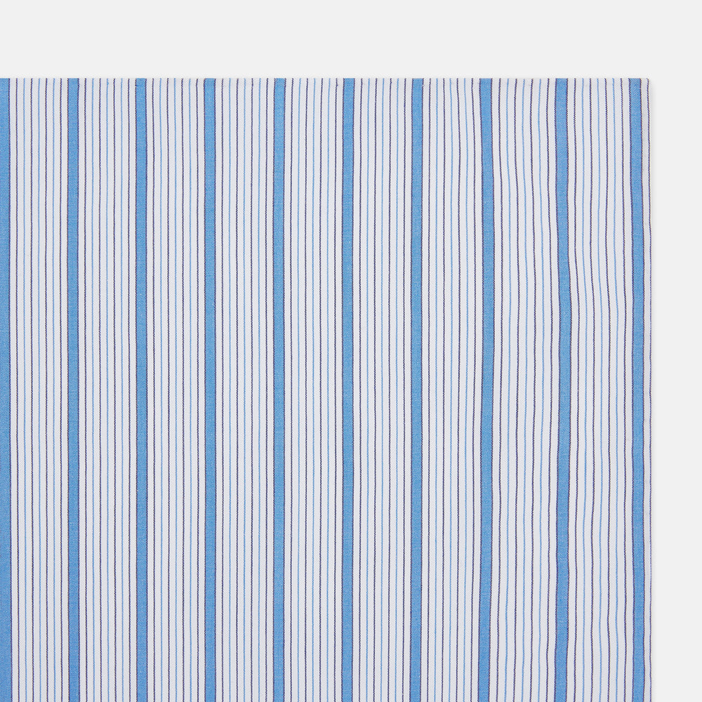 The Hand Rolled Blue Multi Track Stripe Handkerchief by Turnbull & Asser features a square white design with vertical light blue and navy stripes of varying widths—a timeless gentleman’s accessory.