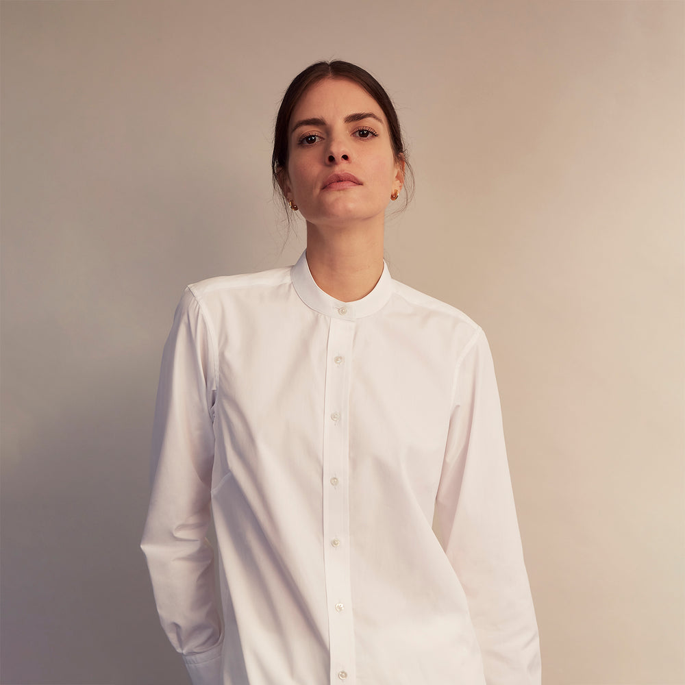 The White Cotton Lauren Shirt by Turnbull & Asser, featuring a stand collar, button-down front, and elongated body, is laid flat on a plain white background.