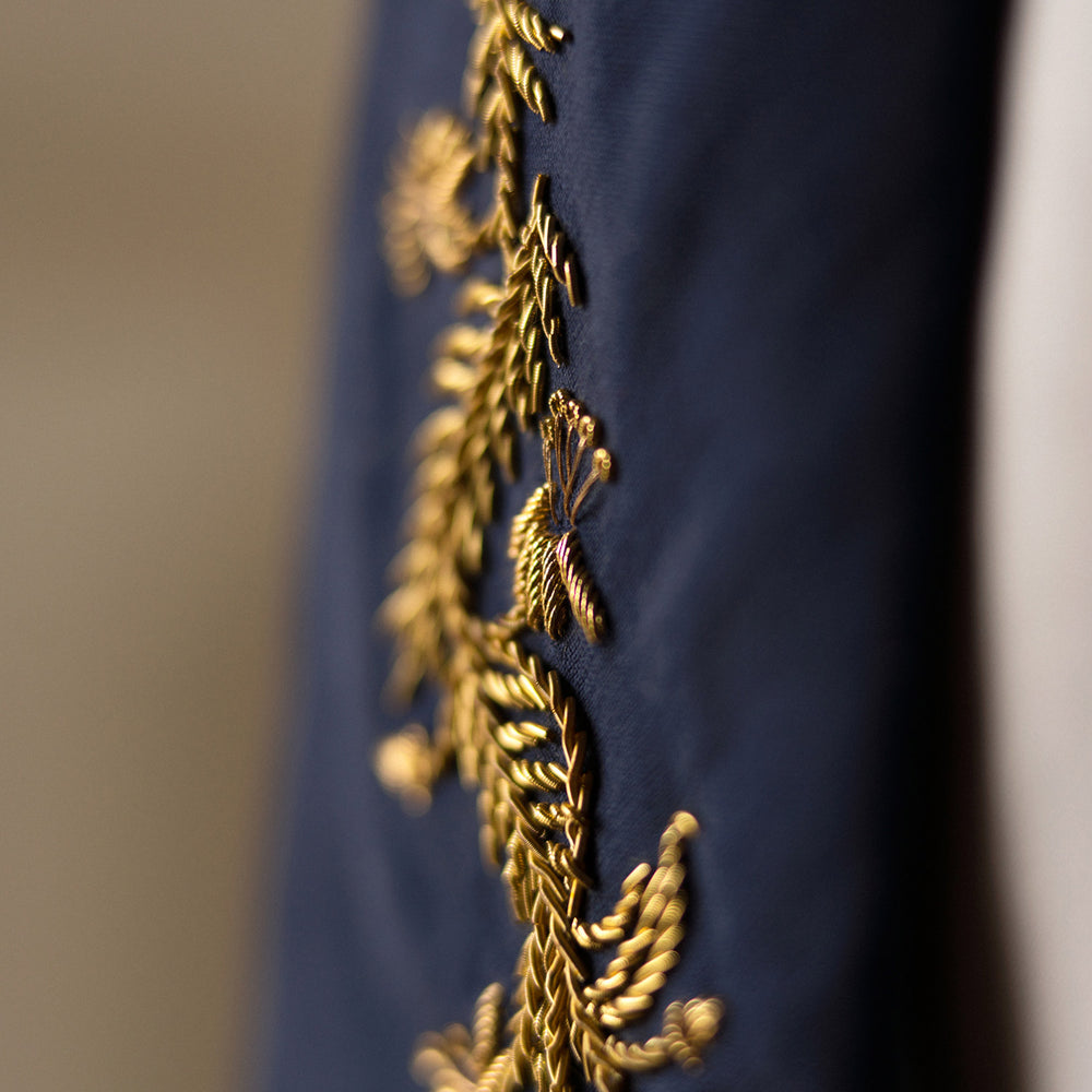 The Turnbull & Asser Navy Gold Embroidered Botanical Tie features intricate gold botanical embroidery on navy blue silk, neatly rolled with the detailed tip facing forward.