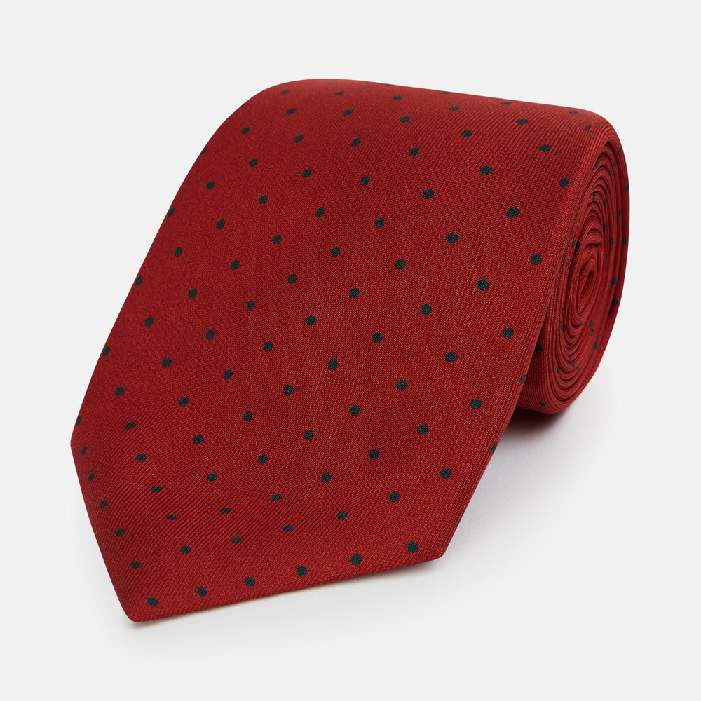 The Turnbull & Asser Red and Navy Polka Dot Silk Tie is elegantly rolled on a white background, highlighting classic British craftsmanship.