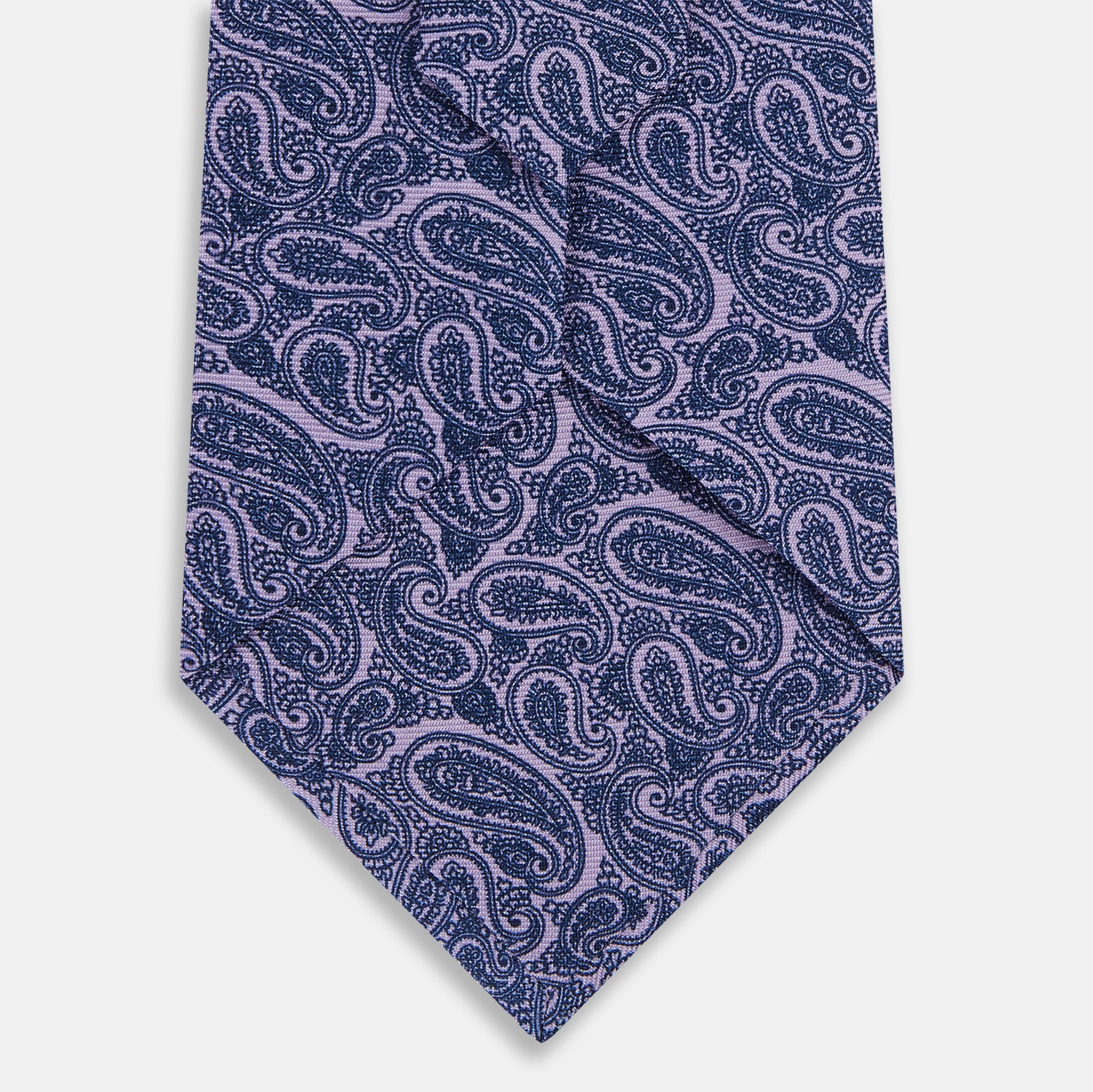 View 3 of product The Turnbull & Asser Lilac Paisley Silk Tie is shown rolled up, featuring a blue paisley pattern on a light purple background and displayed on a white surface.