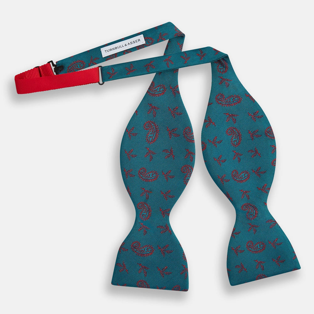 The Turnbull & Asser Teal Paisley Silk Bow Tie, featuring a red paisley and bee pattern, adds a touch of British elegance and formal refinement to your ensemble.
