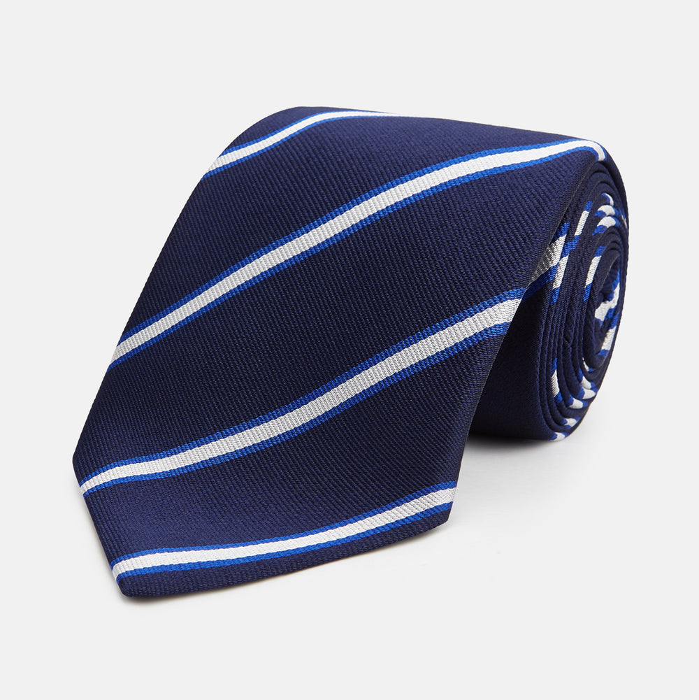 The White and Navy Blazer Silk Tie by Turnbull & Asser features diagonal white and light blue stripes on navy silk, shown rolled on a white background. A refined choice to complement any office shirt.