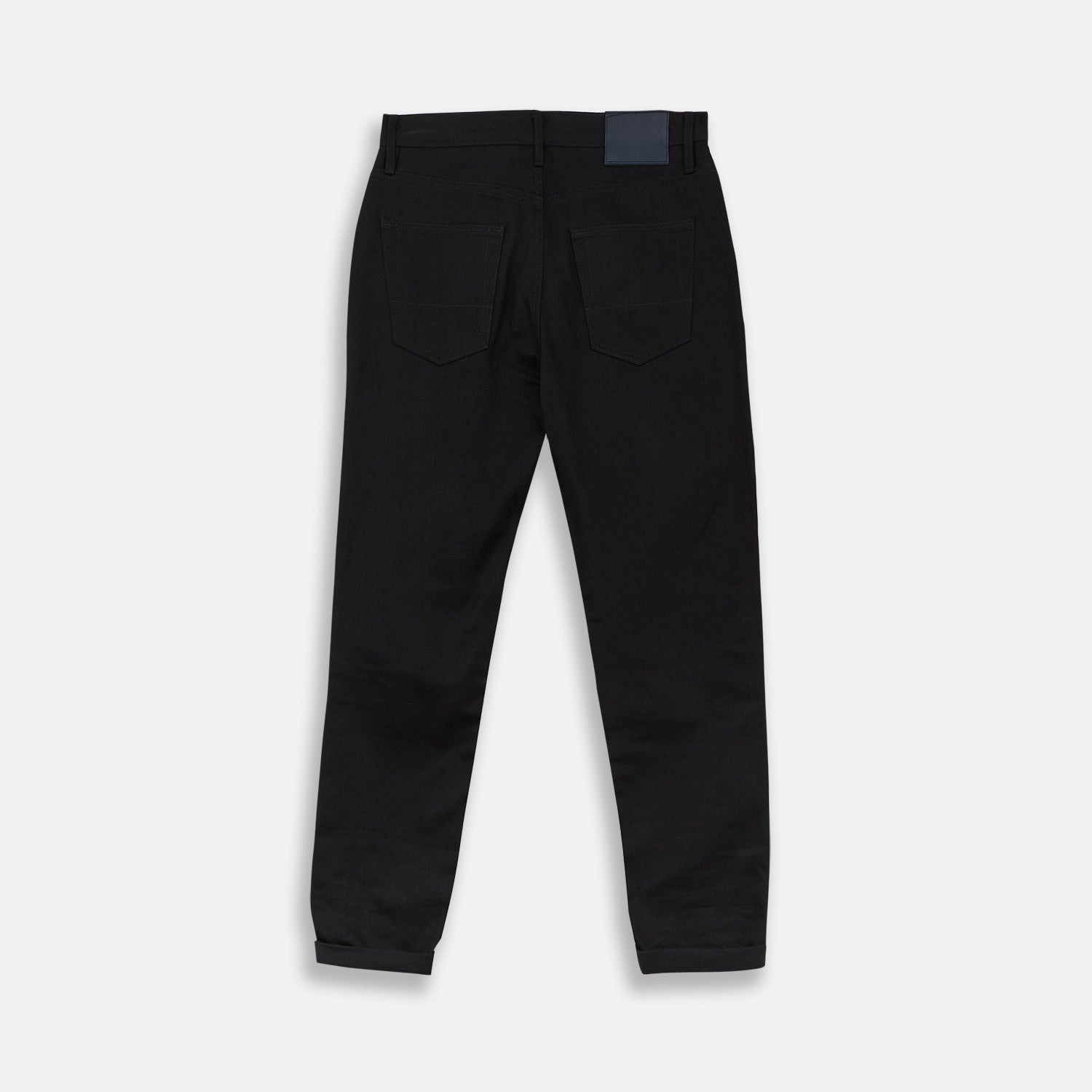 View 3 of product A pair of Turnbull & Asser Black Italian Selvedge Denim Jeans with a five-pocket design, button closure, and cuffed hems, displayed flat on a white background.