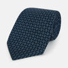 View 1 of product The Turnbull & Asser Navy Floral Silk Tie is crafted from fine English silk, featuring a repeating pattern of small white circular floral motifs, and is neatly rolled for display against a plain white background.