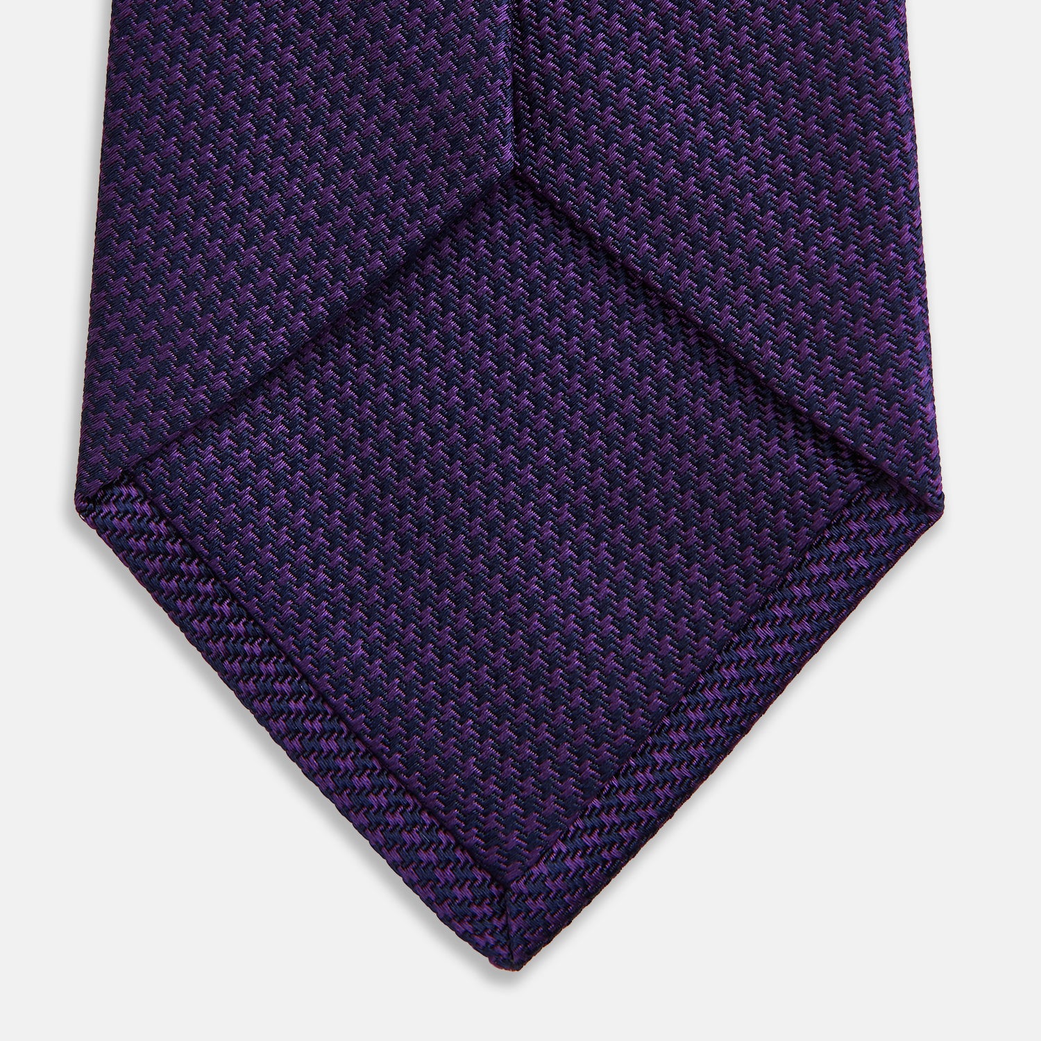 View 4 of product The HOUNDSTOOTH NAVY PLUM TIE by Turnbull & Asser, featuring a textured pattern, is showcased rolled up against a plain white background—an essential accessory.