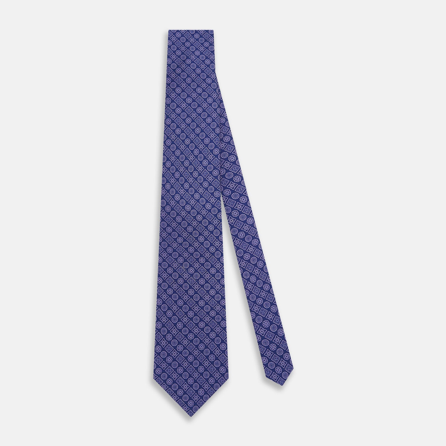 View 2 of product The Turnbull & Asser Azzurro Floral Tile Pattern Printed Silk Tie features blue silk with a geometric design of white circles, squares, and floral motifs, displayed on a plain white background.