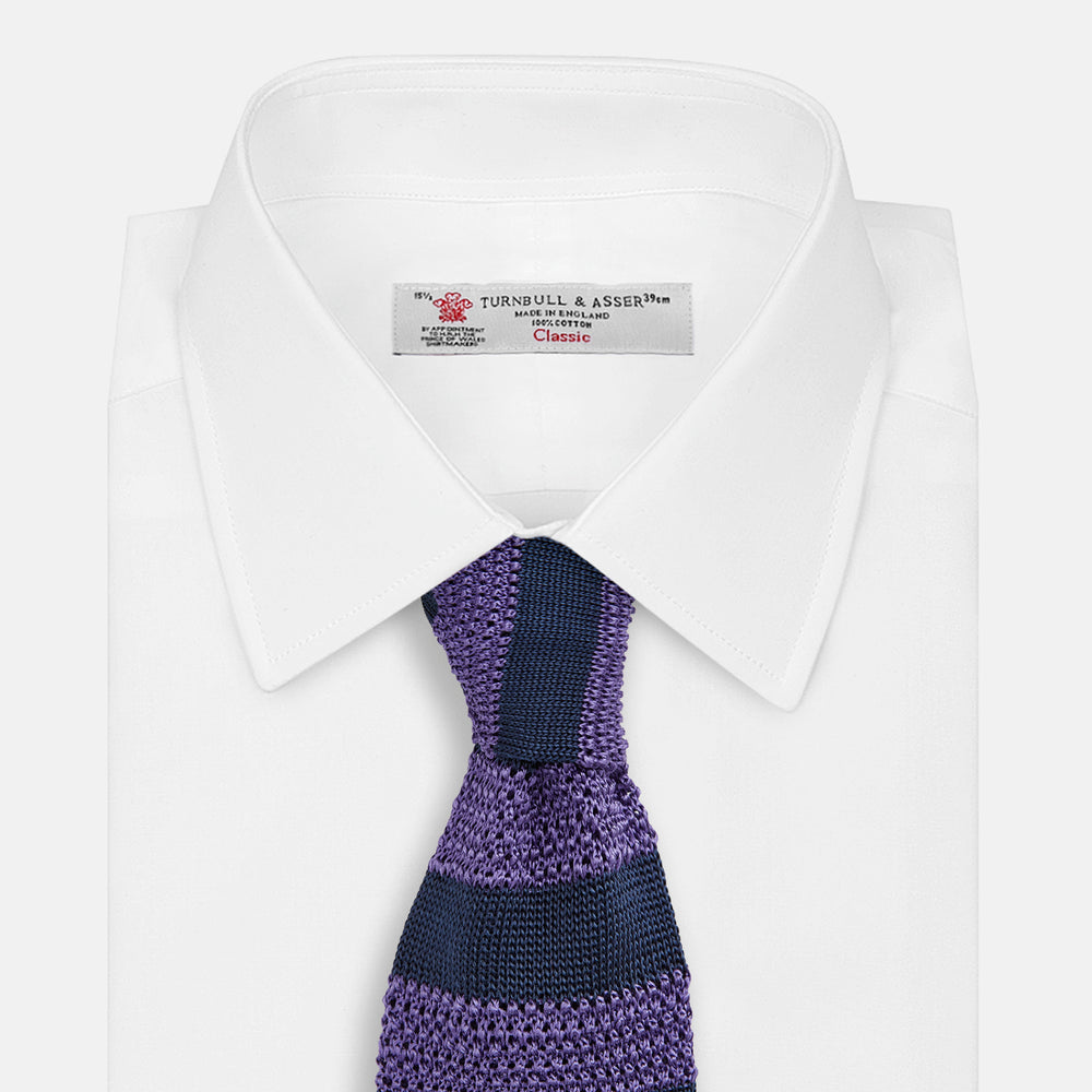 The KNITTED STRIPE PURPLE TIE by Turnbull & Asser features bold dark blue and purple stripes, making it an essential smart accessory. Shown rolled up on a white background.