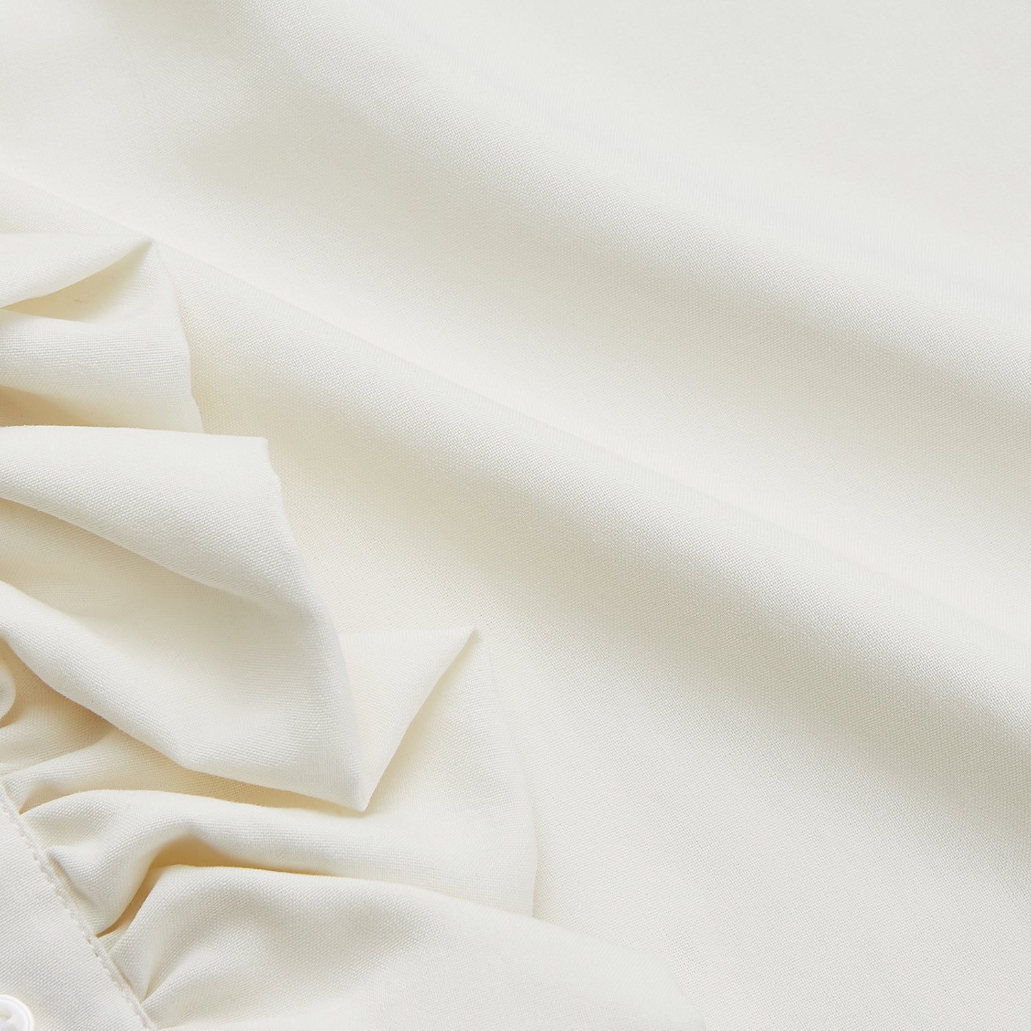 View 5 of product A man in a Cream Silk Regular Fit Ruffle-Front Wilfred Shirt by Turnbull & Asser stands against a dark background, one hand on a chair, gazing thoughtfully to the side.