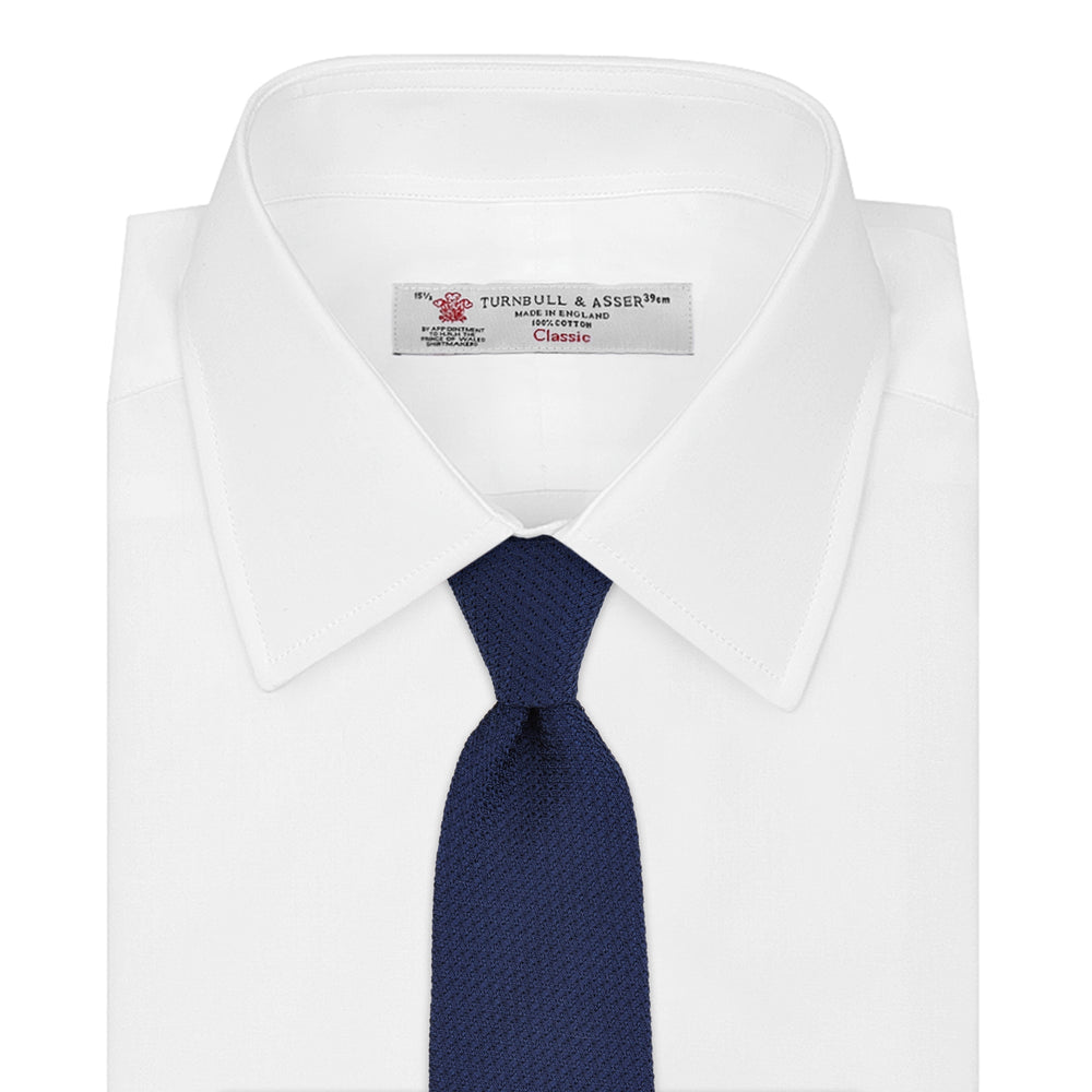 The Turnbull & Asser Plain Woven Grenadine Silk Tie in navy, with a textured finish, is rolled and displayed on a white background—a refined essential for any wardrobe.