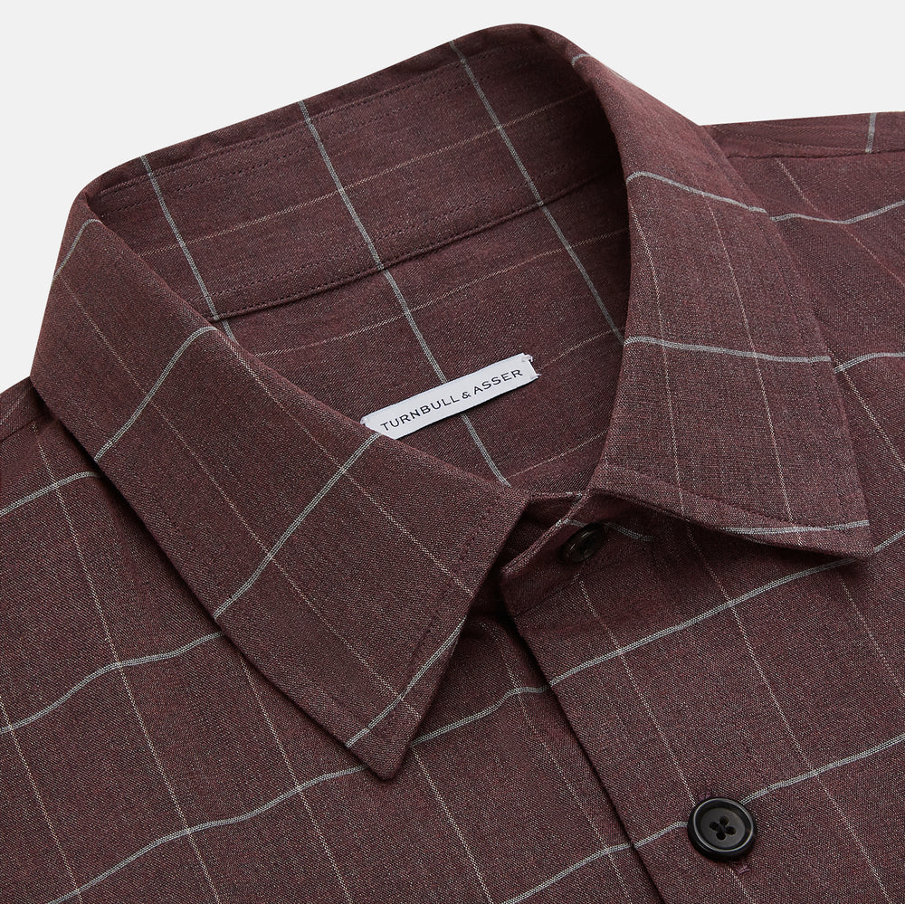 The Turnbull & Asser Burgundy Check Hampstead Overshirt, featuring a button-up front, collar, white windowpane pattern, and two front pockets, is laid flat on a white background—perfect for elegant formal wear.