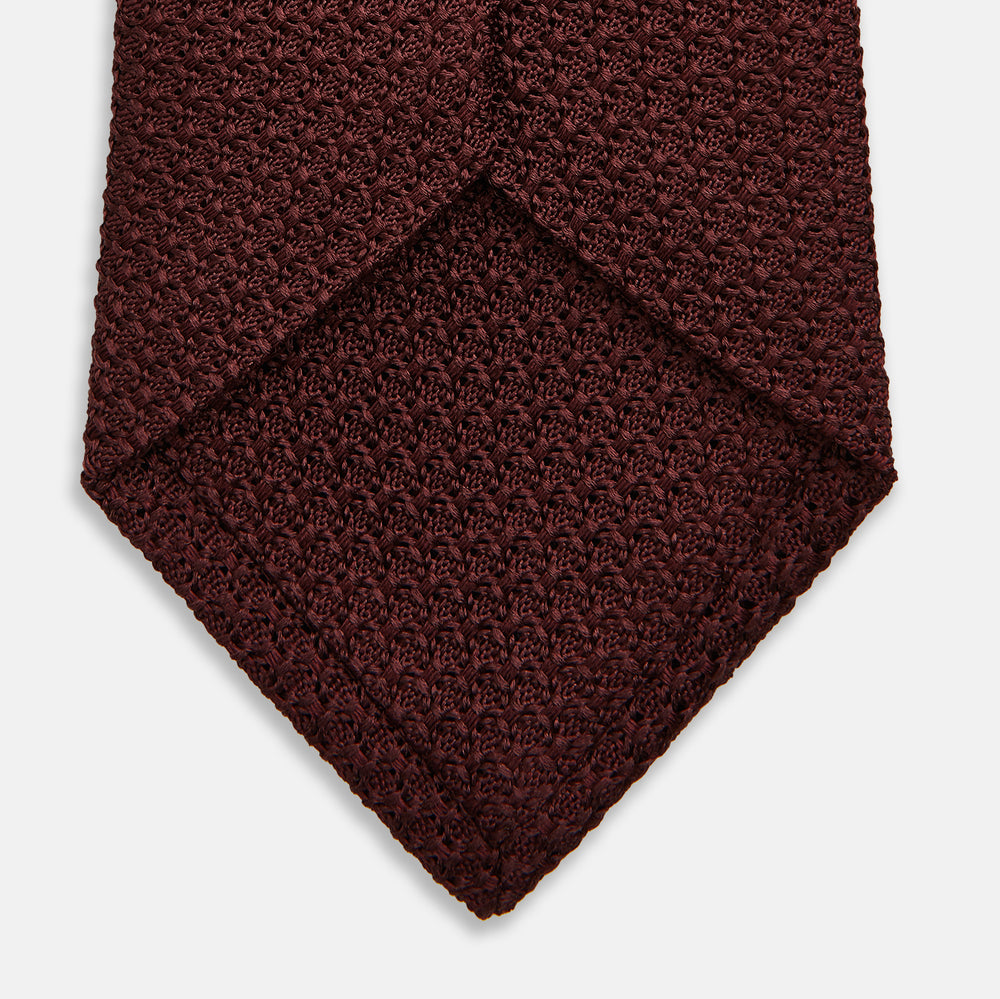 The Turnbull & Asser Burgundy Knitted Tie, rolled and featuring a textured pattern, is displayed on a plain white background—a refined accessory ideal for the modern gentleman’s wardrobe.
