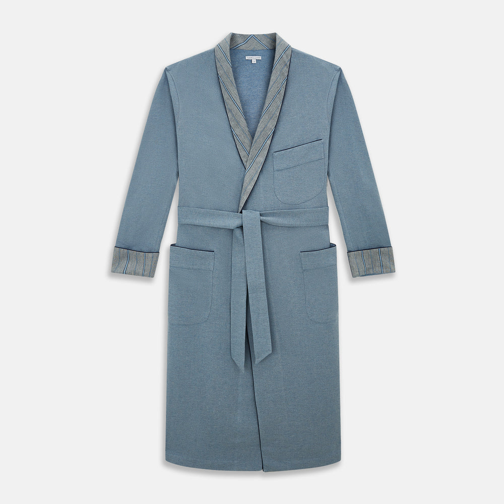 The Turnbull & Asser Blue Stripe Collar Cotton Twill Gown features a light blue hue, striped collar and cuffs, long sleeves, patch pockets, and a matching belt for elevated home comfort. Shown on a white background.