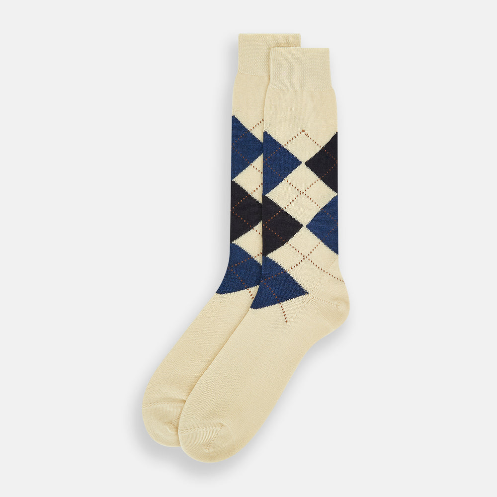 The Turnbull & Asser Vanilla Wool Check Mid-Length Sock is beige with blue, black, and white argyle diamonds on the side and solid beige toe, heel, and cuff. Displayed on a plain white background.