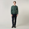 View 1 of product A man stands facing the camera against a plain light background, wearing the Turnbull & Asser Bottle Green Merino Kingston Crew Neck Jumper with dark pants and black shoes. His arms rest at his sides and he has a neutral expression.