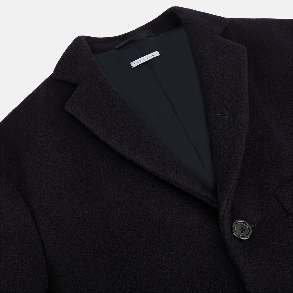 The Navy Apsley Single-Breasted Caban Coat by Turnbull & Asser features three buttons, notch lapels, a chest pocket, and two front flap pockets, shown against a plain light gray background.