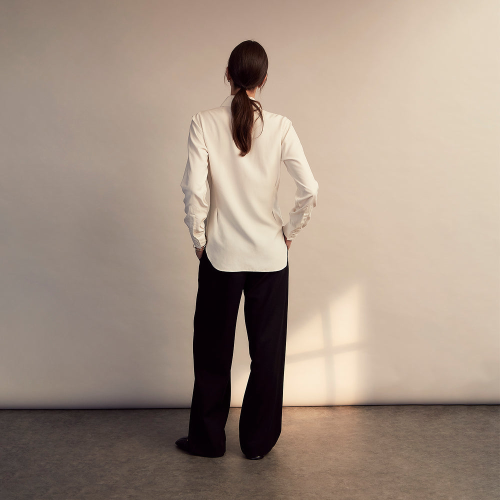 The Cream Silk Tailored Bianca Shirt by Turnbull & Asser features long sleeves, a pointed collar, and curved hem in soft-touch peace silk with a tailored fit. Shown laid flat on a white background.