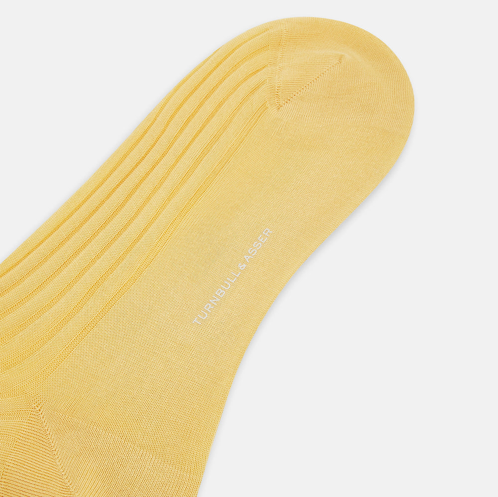 The Turnbull & Asser Banana Long Socks are knee-high, golden-yellow, and made from mercerised Egyptian cotton, shown upright on a white background to highlight their ribbed texture and fitted shape.