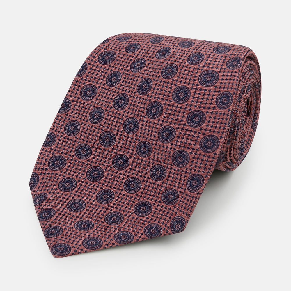 The Turnbull & Asser Antique Pink Medallion Silk Tie features a rolled-up design with small dark blue circular motifs on a white background.