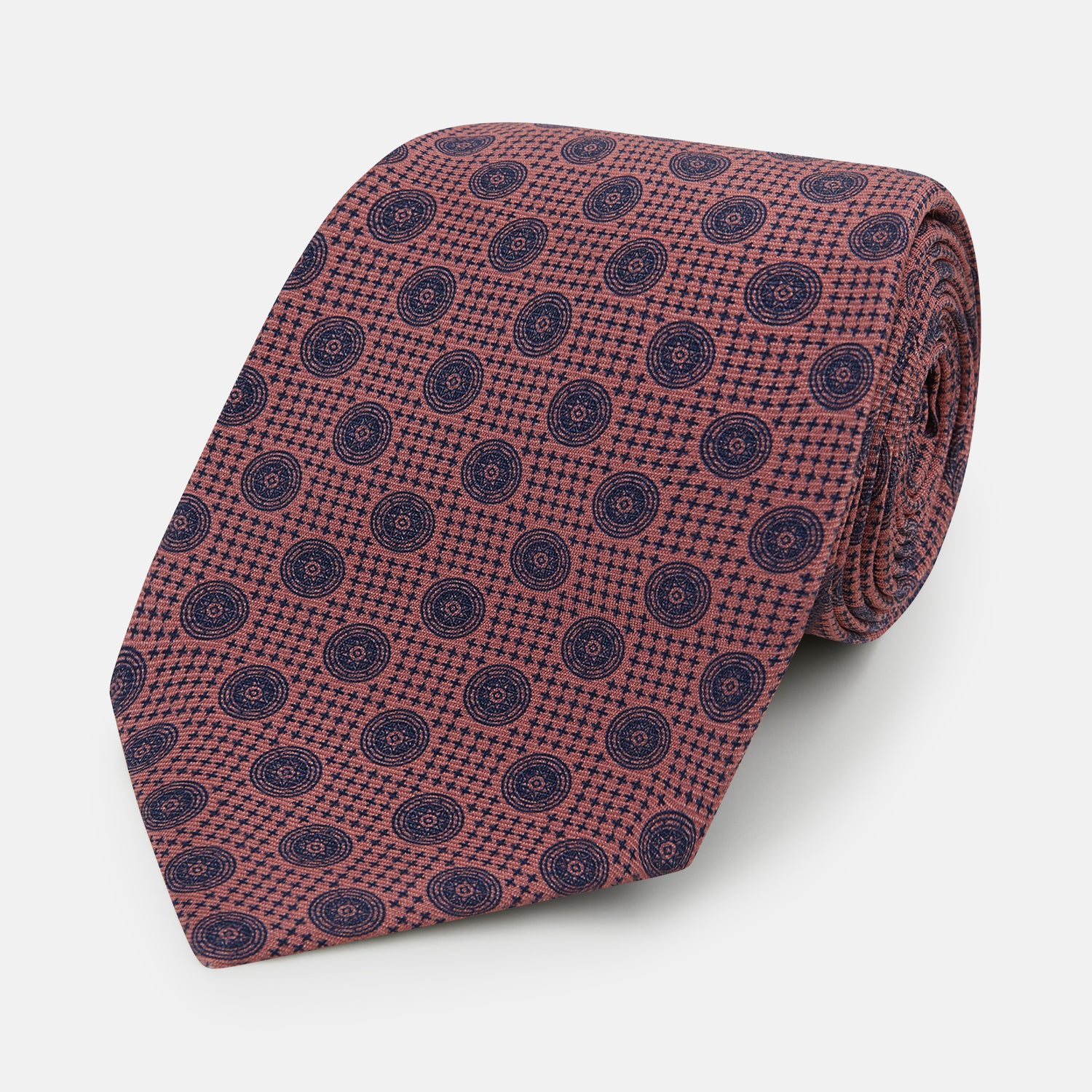 View 1 of product The Turnbull & Asser Antique Pink Medallion Silk Tie features a rolled-up design with small dark blue circular motifs on a white background.
