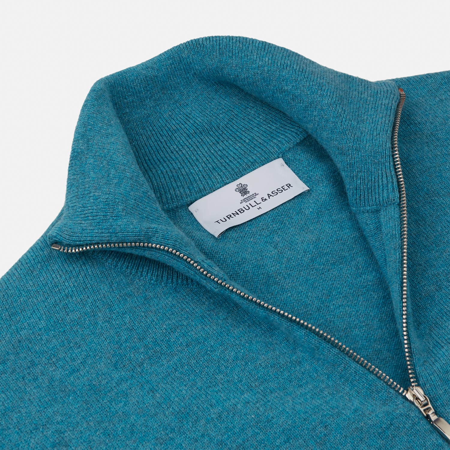 View 2 of product The Teal Lennox Half-Zip Jumper by Turnbull & Asser features a quarter-zip front, long sleeves, high collar, and ribbed cuffs and hem, shown laid flat on a light background.