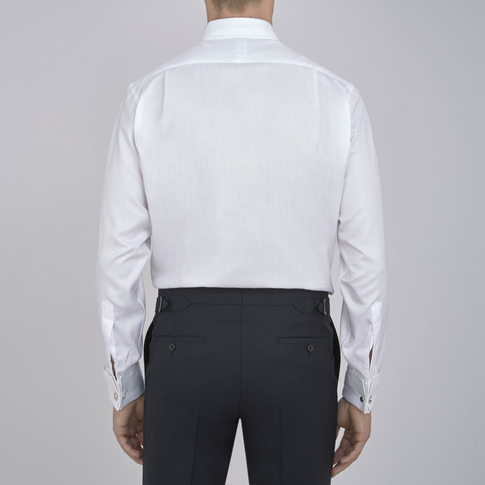 The Turnbull & Asser White Herringbone Superfine Cotton Shirt features a T&A collar, double cuffs, and a visible label inside the collar, shown neatly folded on a light blue background—ideal for minimalist looks or pairing with bold ties.