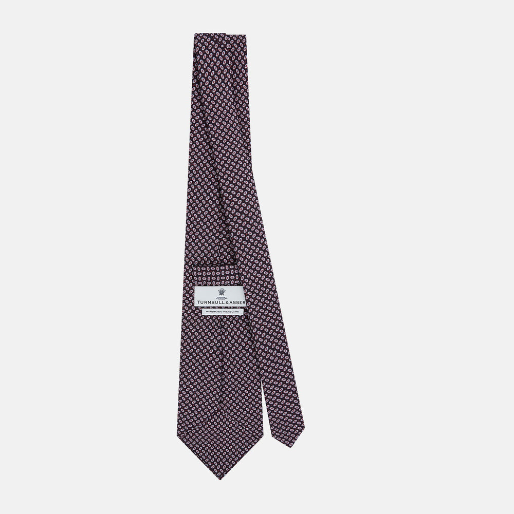 The Turnbull & Asser Red and Navy Oval-Patterned Silk Tie features a refined oval motif on navy silk, ideal for formal wear, and is showcased on a plain white background.