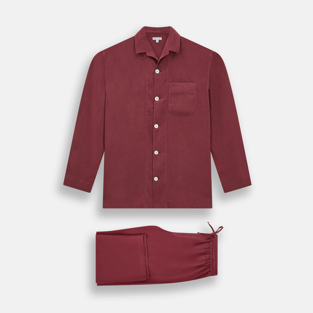 The Turnbull & Asser Burgundy Silk Pyjama Set features a long-sleeve, button-up shirt with chest pocket and matching pants with elastic waistband and side pocket, shown on a white background.
