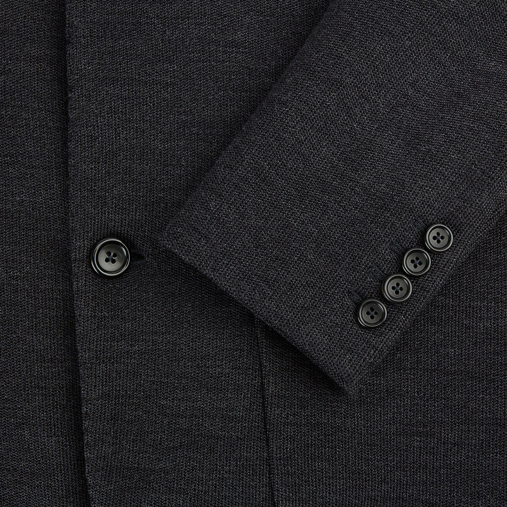 The Turnbull & Asser Charcoal Knitted Oxford Blazer features a notched lapel, two-button closure, and three front pockets, blending modern elegance with British heritage against a plain white background.