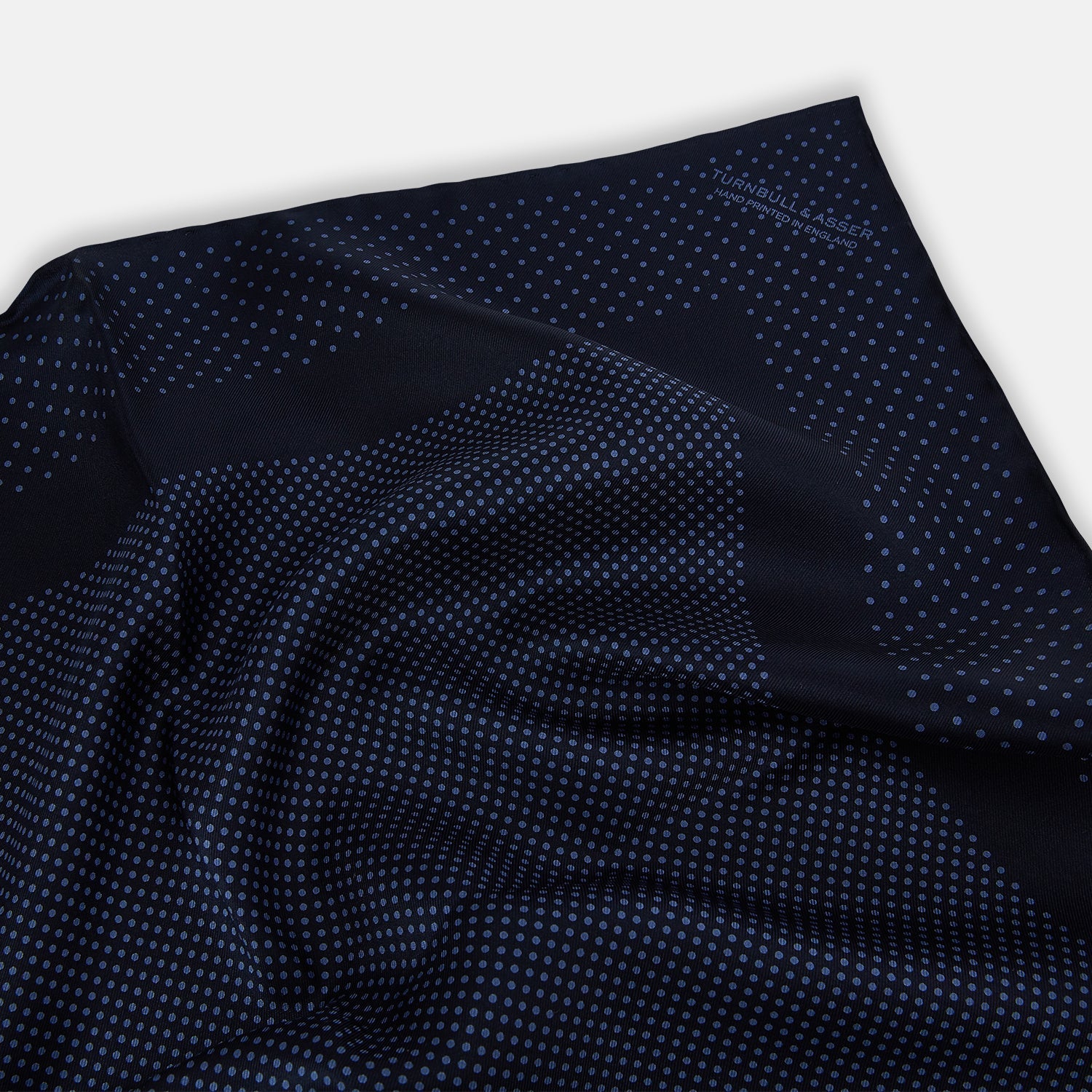 View 2 of product The Turnbull & Asser Midnight Blue Dot Silk Pocket Square features a neatly folded, handmade design with small light blue polka dots and a plain border.