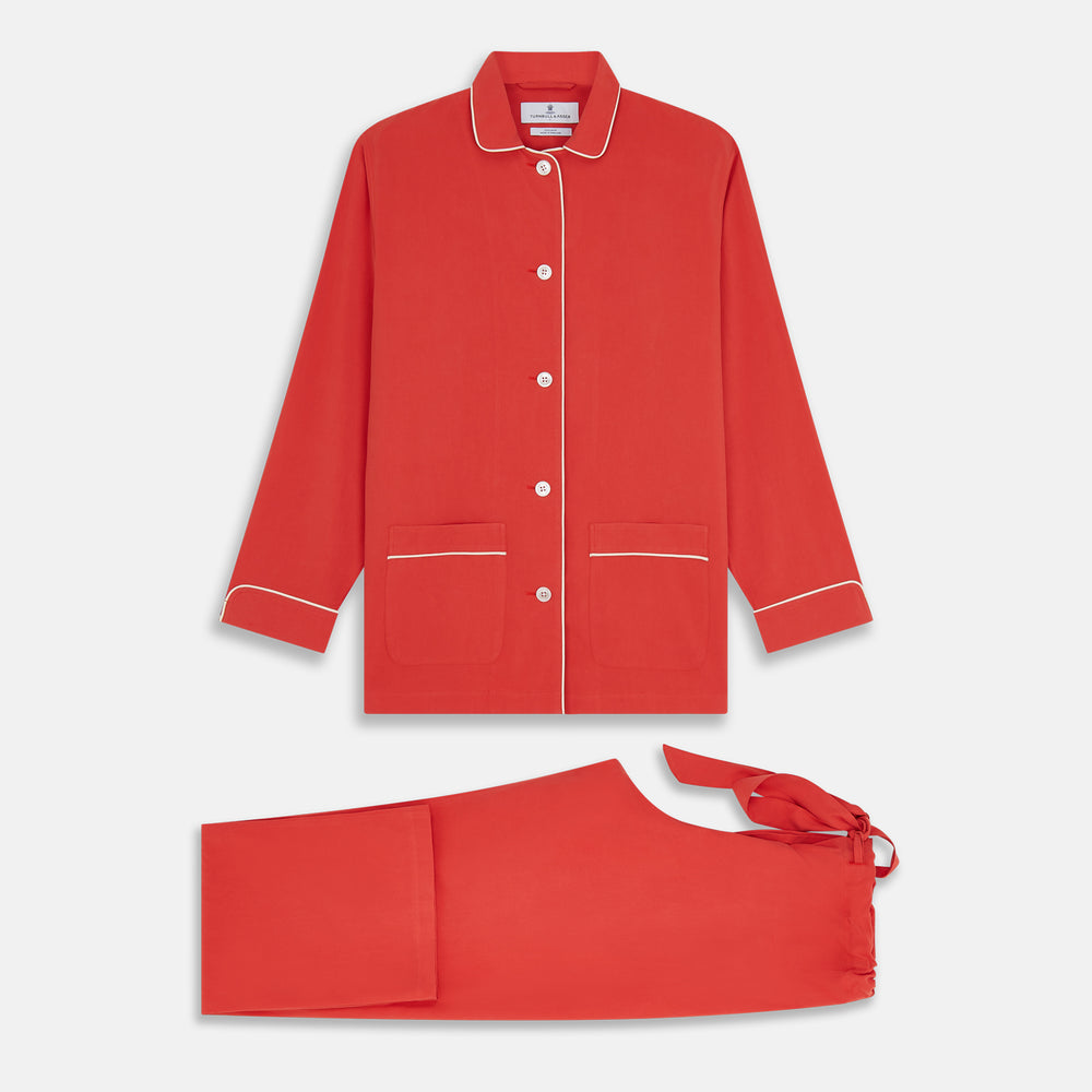 The Turnbull & Asser Women's Coral Pink Silk Thelma Pyjama Set features a long-sleeve button-up top with two front pockets and matching drawstring pants, shown on a white background.