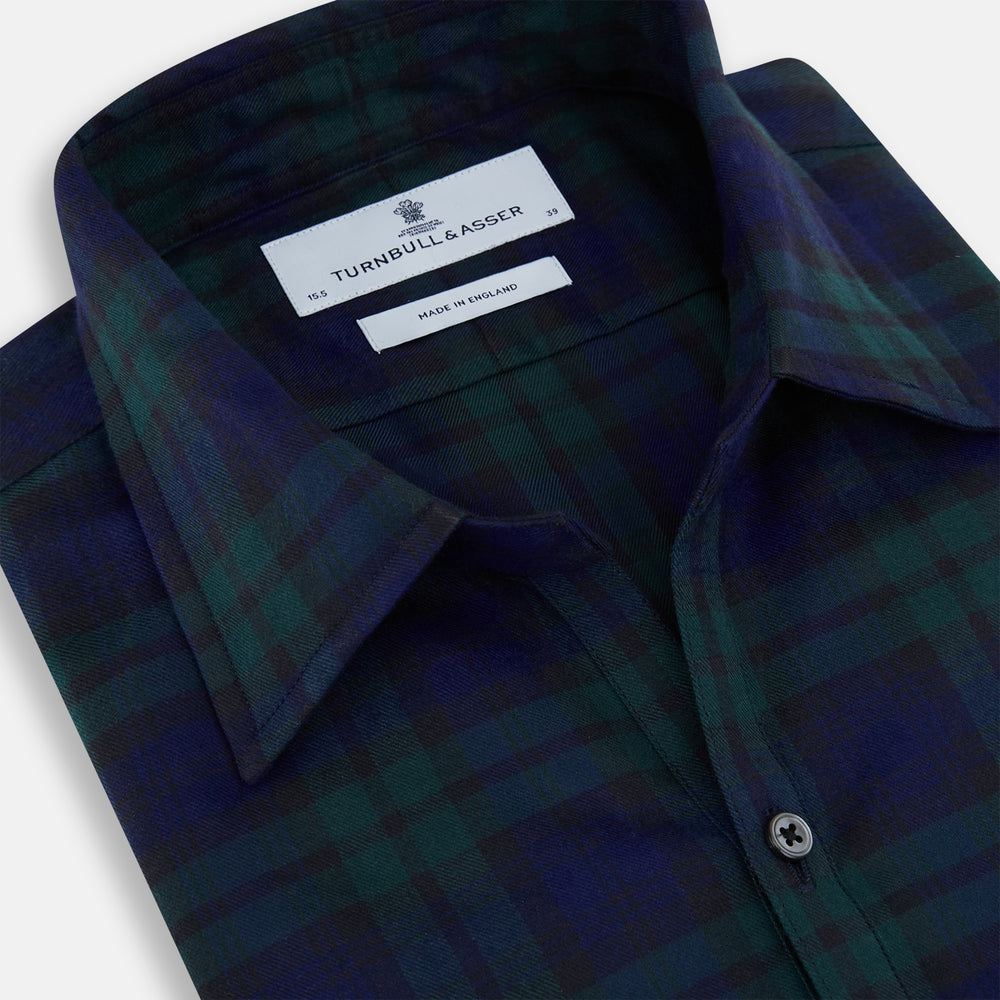 The Turnbull & Asser Black Watch Tartan Windsor Shirt is a long-sleeve, button-up shirt with a dark green and navy tartan pattern, white buttons, collar, and curved hem—showcasing British craftsmanship on a plain white background.