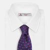 View 2 of product The Turnbull & Asser MINI SQUARE SPOT PLUM BLUE TIE is a luxury English silk necktie in plum, featuring a blue and white grid pattern of small squares, displayed rolled up against a simple light background.