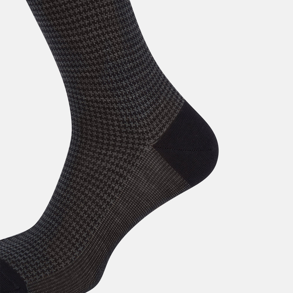 The Turnbull & Asser Charcoal Melange Houndstooth Long Sock is knee-high, with a subtle dark houndstooth pattern and solid black toe, heel, and cuff, shown on a white background.